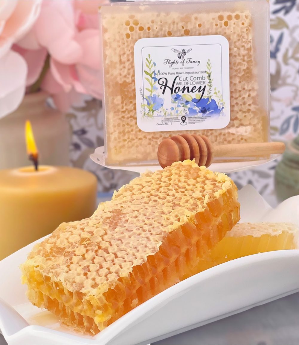 Pieces of cut comb honey on a white dish, with a boxed comb and a beeswax candle behind.